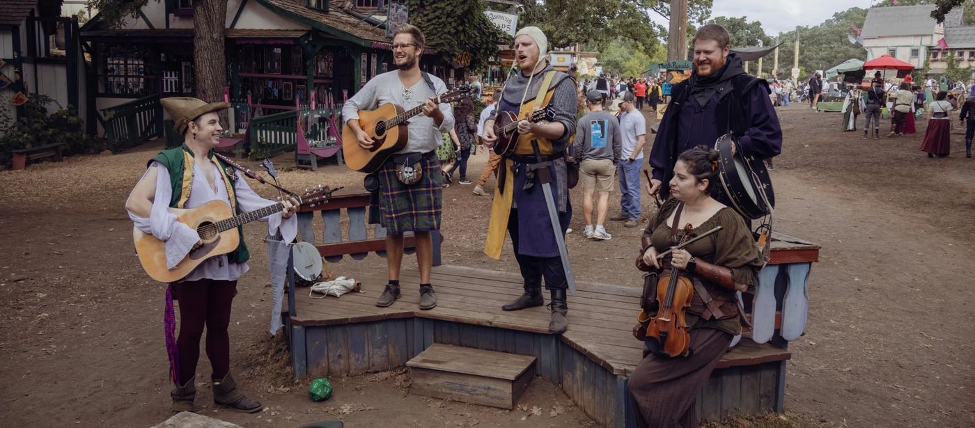The five members of the band playing on a small wooden stage at the Minnesota Renaissance Festival.